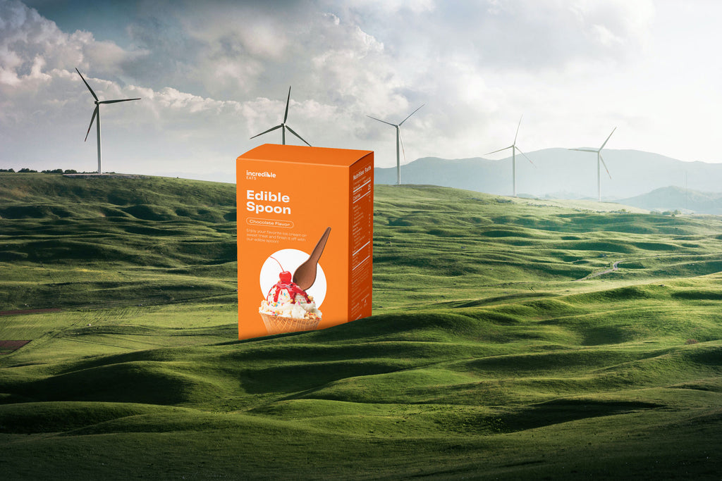 A photo of the Chocolate Spoons orange box in a green field with wind turbines in the background. 